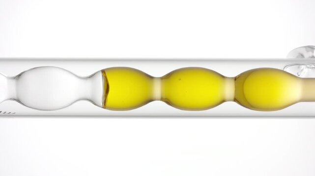 Big close vertical shot of air bubbles racing through clear yellow liquid as it fills and drains from a bulb lab condenser set over a white background | Collagen liquid cosmetic formulation concept