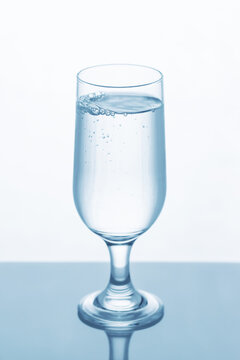 A glass of clean liquid placed on a transparent surface, reflecting its image