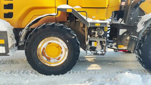 Heavy yellow front-end loader parked outdoors on snowy ground with bucket full of snow, machine used for clearing snow, winter scene, construction equipment, large vehicle