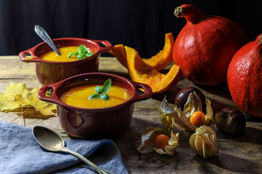 Pumpkin or butternut squash soup in bowls with autumn leaf, gooseberry in dark and moody background.