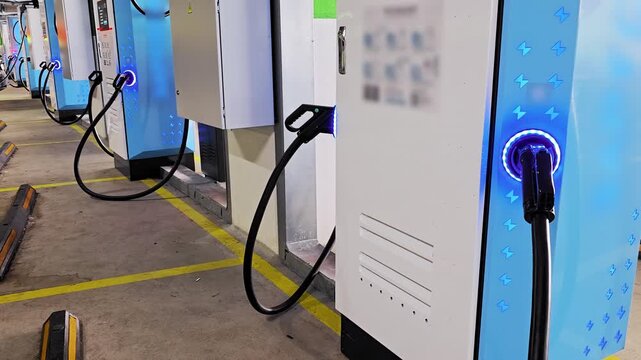 Electric vehicle charging stations illuminated with blue light in indoor parking garage, row of modern sustainable energy infrastructure for urban transport of future