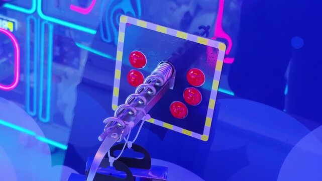 Close-up view of a vibrant game control panel featuring a metallic spring-loaded lever and six illuminated red buttons in an arcade setting with neon lights