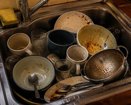 Dirty used kitchen dishes piled in a metal sink at home
