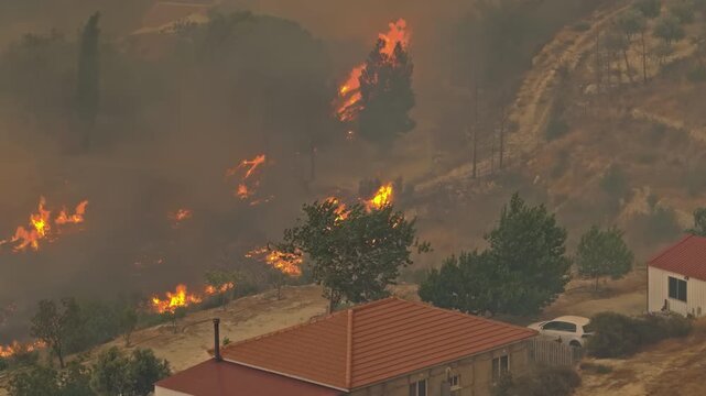 Wildfire advancing dangerously toward homes on a hillside.
