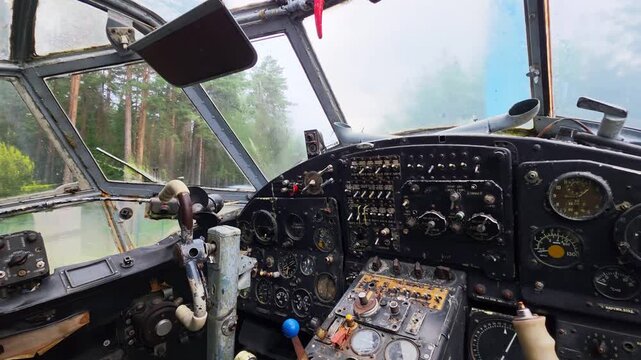 Interior view of old airplane cockpit showing instrument panel and pilot controls, a vast forest visible through front windshield, a scene suggesting aviation history and abandonment