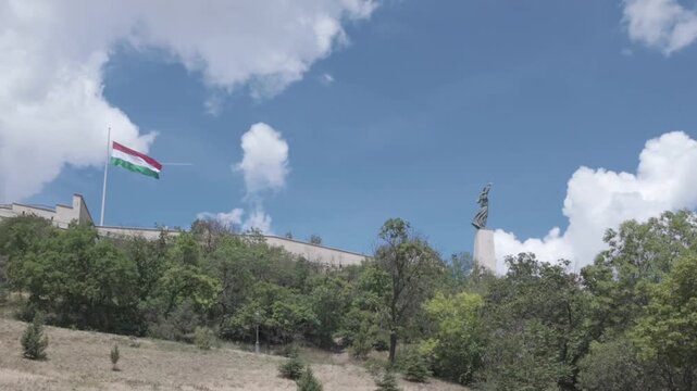 4K video of a fortress with a large freedom statue and a Hungarian flag on Gellert Hill in Budapest, Hungary