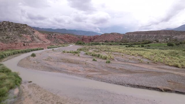 4K drone aerial view of La Poma, Salta, Argentina. Stunning Andean landscape with red rock mountains, green valleys and a river crossing the dramatic canyon scenery.