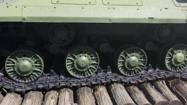 Military tank track wheels detail, heavy armored vehicle part, olive green metal construction, powerful continuous track system, parked on wooden log platform, war machine.