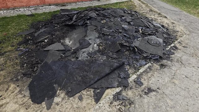 Pile of old roofing felt and bitumen debris removed from a roof during renovation project. Construction waste material on ground after repair of a multi-story building.