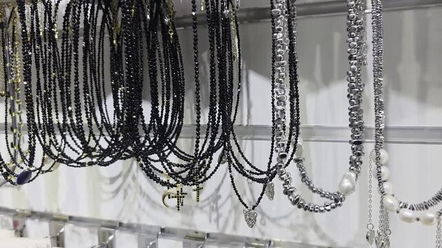 Assortment of necklaces hanging on display rack in retail store, featuring black beaded designs with cross and crescent moon pendants, alongside silver-colored and pearl-like necklaces