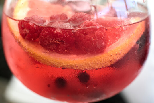 Close-up view of a refreshing pink gin cocktail garnished with fresh raspberries and citrus slices