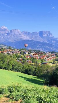 Hot air balloon flying over scenic mountain village and alpine landscape under clear blue sky