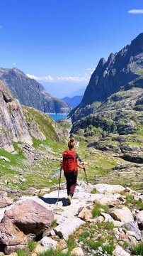 Woman hiker with backpack walking along mountain trail towards alpine lake under clear blue sky, Swiss Alps mountain and Emosson lake.