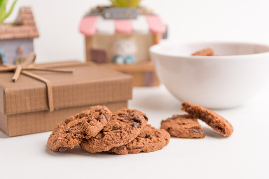 Chocolate chip cookies with brown gift box and small decorative plants arranged on white background