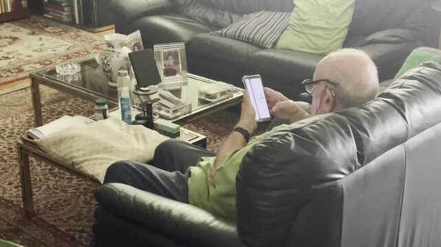 Mayor con tel&eacute;fono m&oacute;vil anciano sentado en sof&aacute; de sal&oacute;n de casa abuelo con smartphone viejo pelo blanco y calvo usando celular