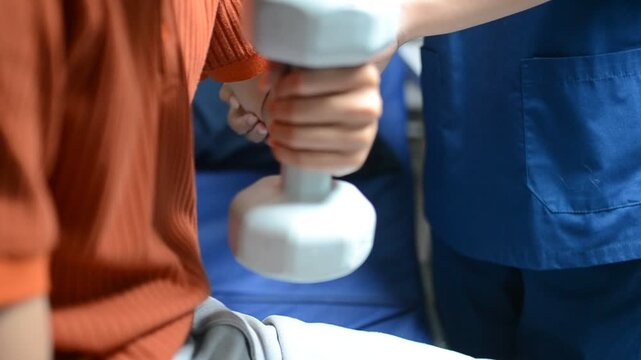 Physical therapist guides male patient using dumbbells for strength training. Person works out arm muscles in clinic. Patient performs rehabilitation exercises for recovery and mobility.