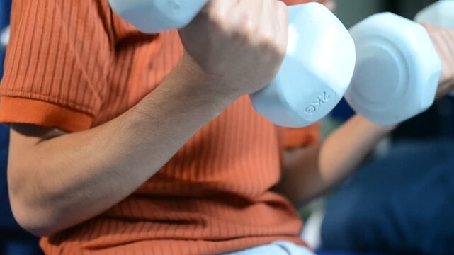 Physical therapist guides male patient using dumbbells for strength training. Person works out arm muscles in clinic. Patient performs rehabilitation exercises for recovery and mobility.