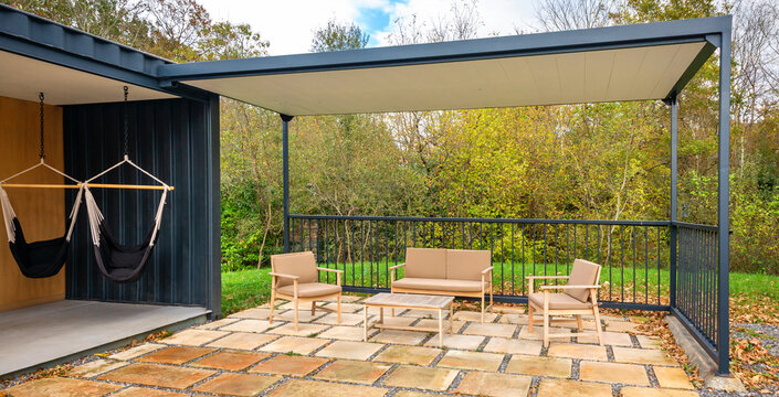 Outdoor living space built from recycled shipping containers featuring a modern pergola covering patio furniture and lounge area with hammocks, offering relaxation and design surrounded by nature