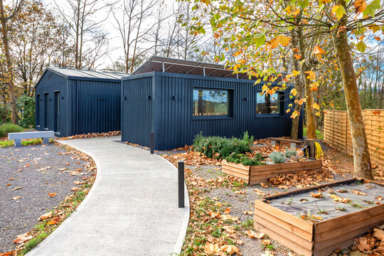 Contemporary modular office constructed from shipping containers with dark facade and rooftop solar panels, pathway and raised garden beds with autumn leaves showcasing eco friendly building in nature