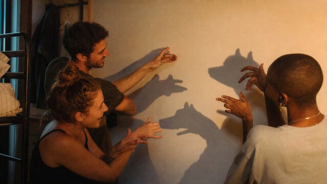 Man and woman playing with hand shadows on hostel wall. Group of friends laughing and making shadow puppets.