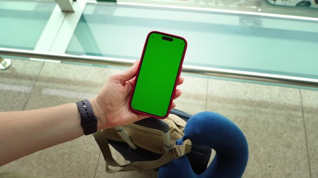 Traveler holding smartphone with green screen while waiting at the airport terminal. High quality 4k footage