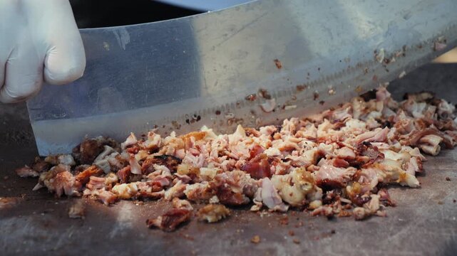 Close-up of a street food vendor chopping seasoned grilled meat on a hot flat-top grill with a large metal cleaver. High quality 4k footage