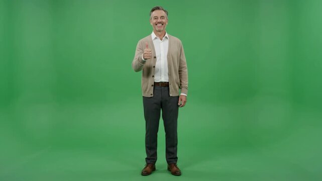 Smiling man in cardigan giving thumbs up on green screen background, full body shot.