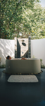 Young woman relaxing in an open-air luxury outdoor bathtub surrounded by green tropical nature at a luxury spa resort