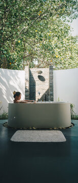 Young woman relaxing in an open-air luxury outdoor bathtub surrounded by green tropical nature at a luxury spa resort