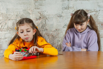 Naklejka premium Two girls sit at a wooden table while one plays with a toy and the other watches with crossed arms