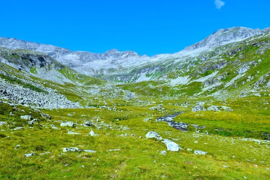 Mountain pasture with a stream and covered in rocks covering P&ouml;llatal valley bellow the mountain peaks in High Tauern, Carinthia, Austria