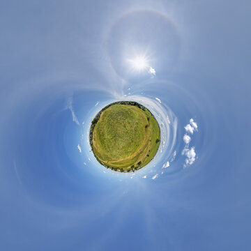 simple little tiny planet without buildings in blue sky with sun and beautiful clouds. Transformation of spherical panorama 360 degrees. Spherical abstract aerial view. Curvature of space.