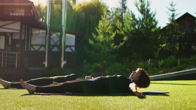 Elderly women practicing gentle outdoor Pilates together on lush grass, performing slow stretching exercises to improve flexibility, balance, and mindful wellbeing