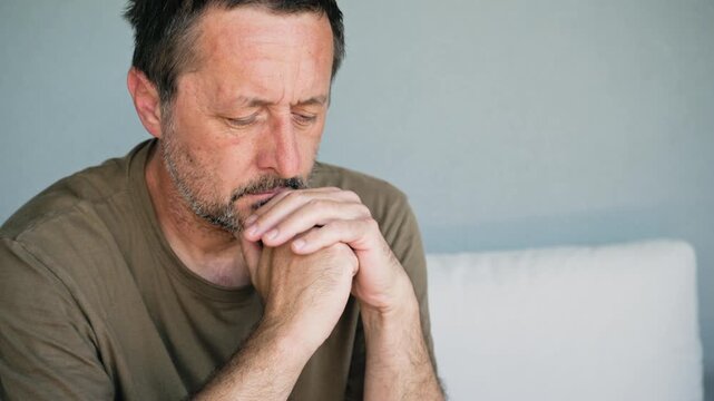 Pensive middle-aged man sitting on sofa deep in thought looking worried and contemplative, rethinking concept, 4K