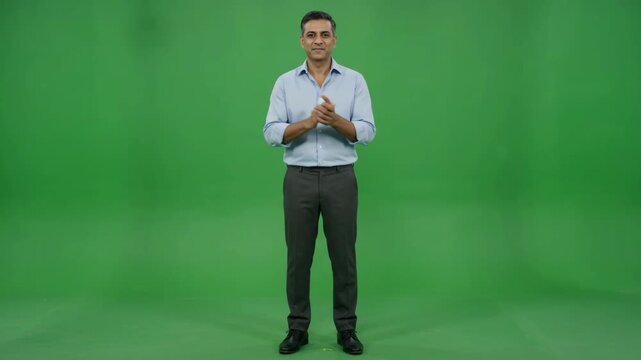 Full shot of a man in a shirt standing against a green screen, clapping his hands.