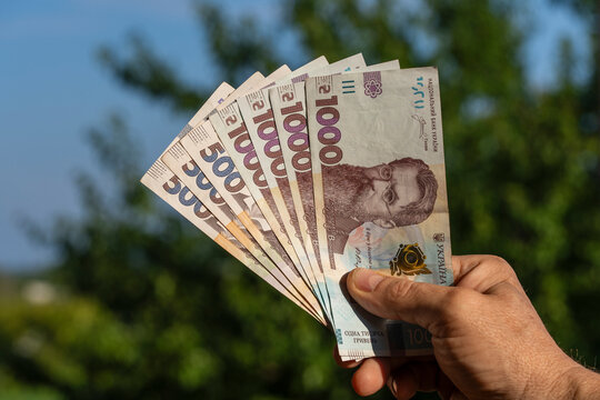 Hand holding Ukrainian hryvnia banknotes outdoors. Closeup of male hand holding fan of Ukrainian cash currency including 1000 and 500 hryvnia banknotes with green nature background