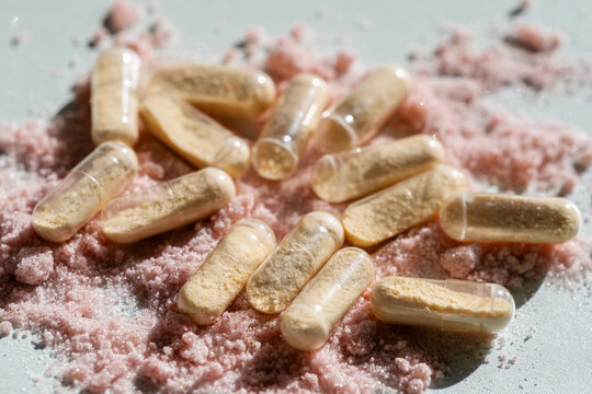 White tablets and capsules arranged over pink powder in a close-up product composition. The image represents pharmaceutical dosage forms, medication, healthcare products and wellness concepts.