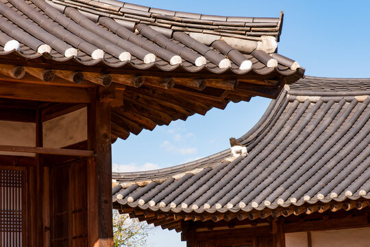 Traditional Korean hanok vernacular architecture horizontal composition featuring curved tiled roofs and wooden eaves against blue sky