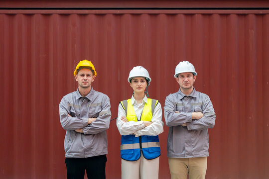 Portrait of professional logistics team with engineer and workers standing with arms crossed in container yard, Multiethnic industrial workers and female supervisor wearing hard hats in shipping port
