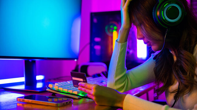 Young Asian woman gamer wearing headphones unset suffer of overspending money from card account after pay game online, problem using credit card