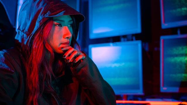 Woman hacker. A woman wearing a hood is thinking looking at a computer monitor. The room is dimly lit. possibly typing or browsing the internet, Hacker in neon light