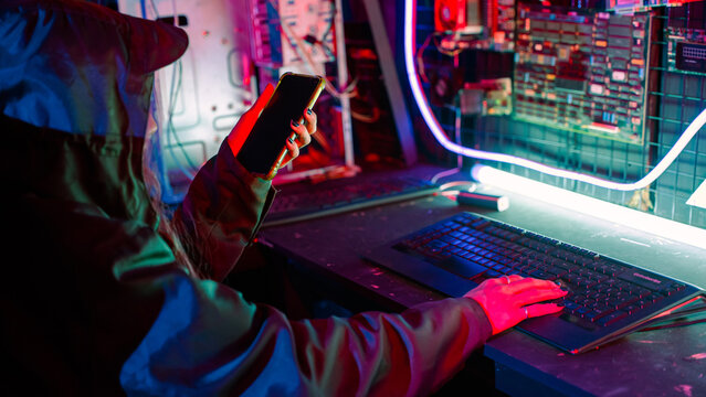 Woman hacker. Asian woman wearing hood working at computer and mobile phone typing coding hacking programming system. Hacker browsing internet uses malware with smartphone to hack password
