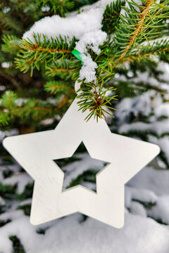 A Christmas tree stands with snow covering its branches. A white star ornament hangs from the tree. The scene captures the holiday spirit and winter atmosphere