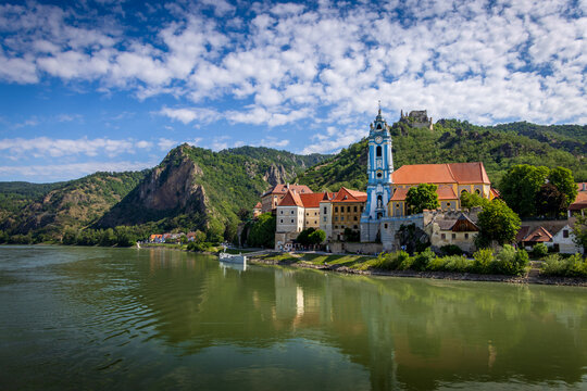 Malerischer Blick auf D&uuml;rnstein in der Wachau mit der blau-wei&szlig;en Stiftskirche und der Burgruine auf dem Berg an der Donau unter beeindruckendem Wolkenhimmel.