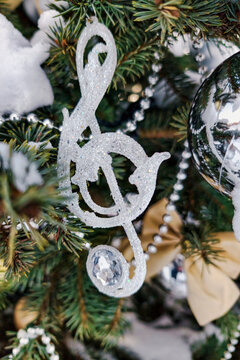 A Christmas tree stands outside in the snow, decorated with ornaments, including a musical note and other shiny items. It is wintertime