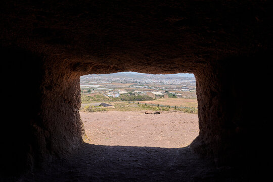 Rectangular stone window framing scenic valley landscape view from interior of Cuatro Puertas cave.