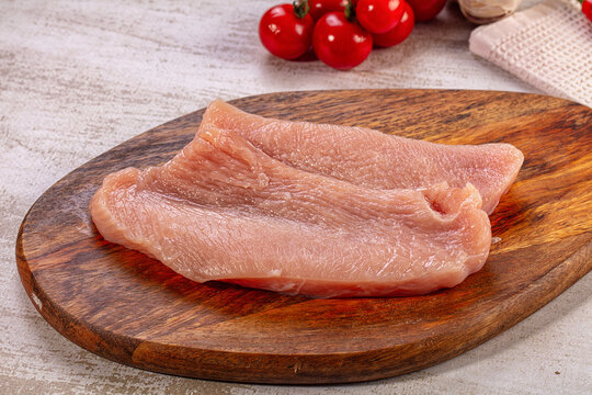 Raw turkey steak on wooden cutting board with cherry tomatoes background