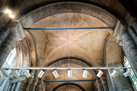 Shallow focus of a row of installed spotlights attached to the ceiling columns as seen in a famous British cathedral. The lights are focused on the souvenir shop area.