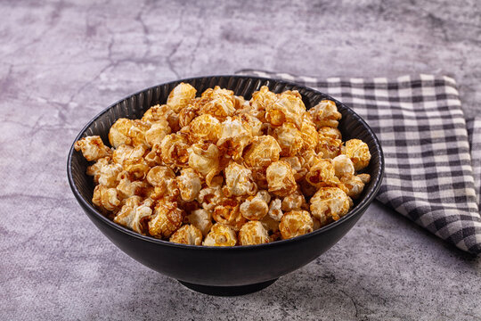 Caramel popcorn in black bowl on gray stone table with checkered napkin