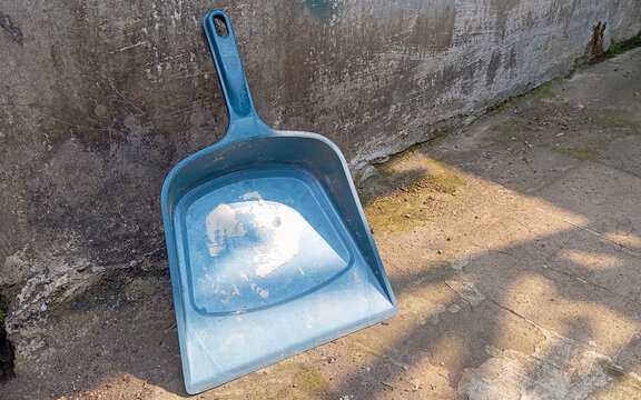 Used Blue Plastic Dustpan Leaning Against a Concrete Wall Outdoors